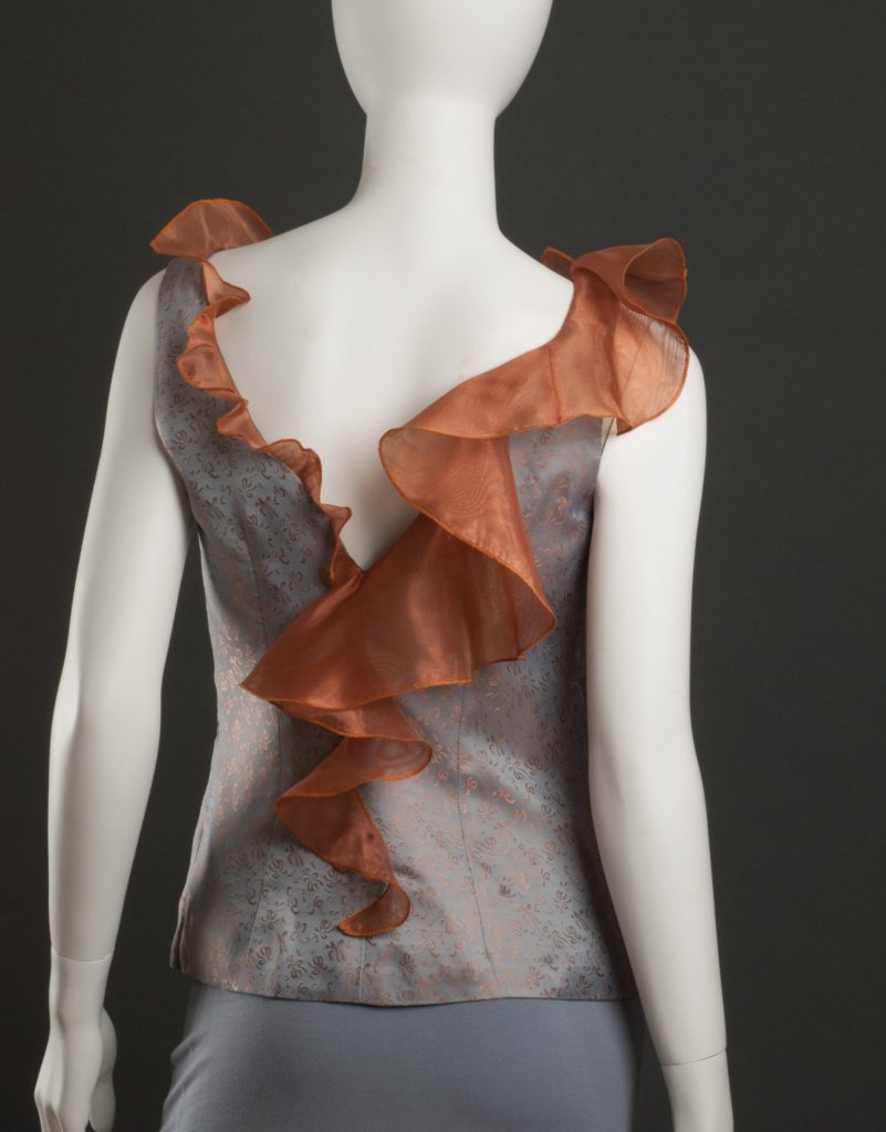 A cinnamon colored flounce encircles the neckline of a woman's bodice, getting larger and more opulent as it circles from center back around to front and back to center back.